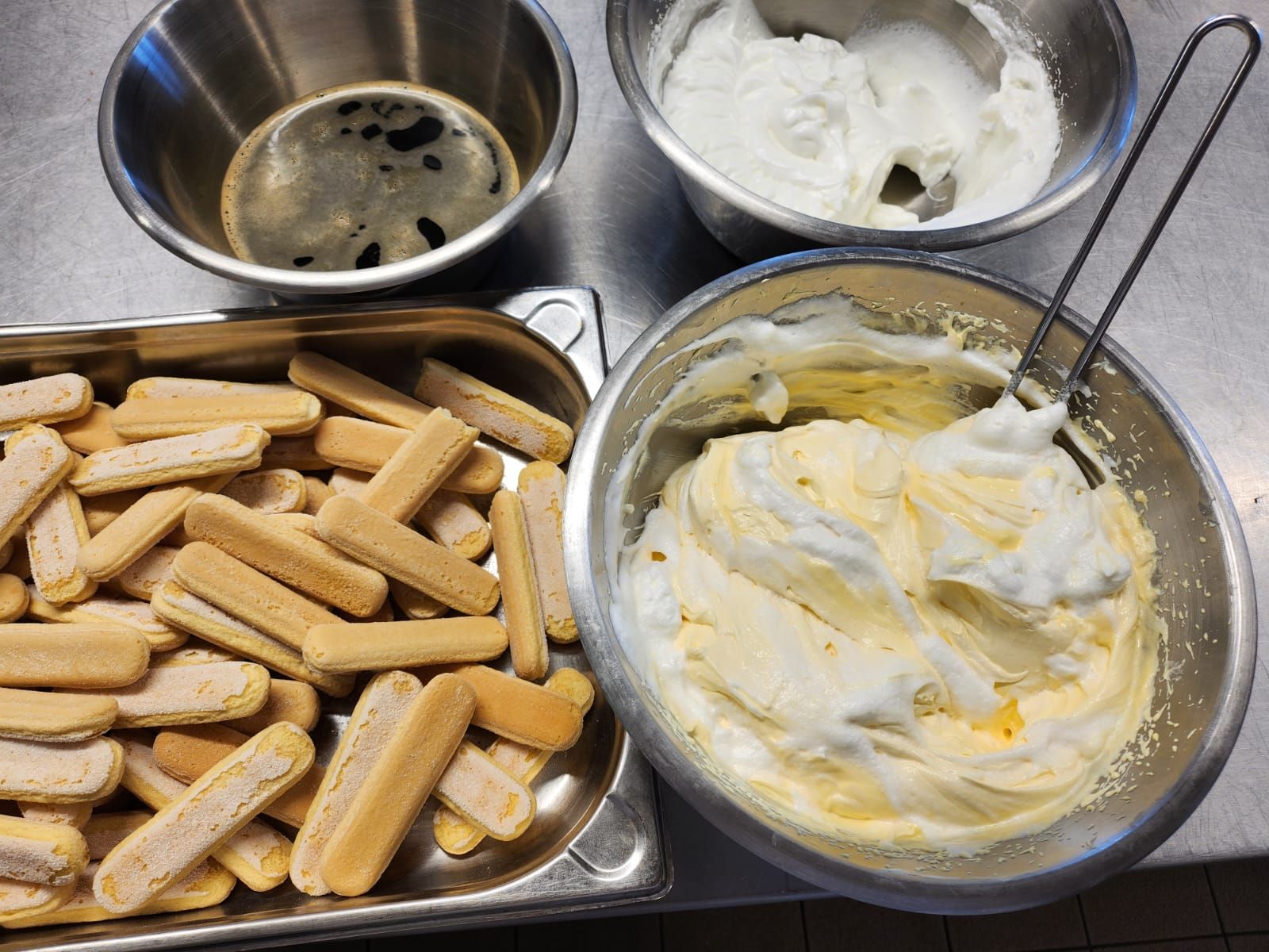 Una bandeja de galletas de tiramisú junto a un bol de crema batida.