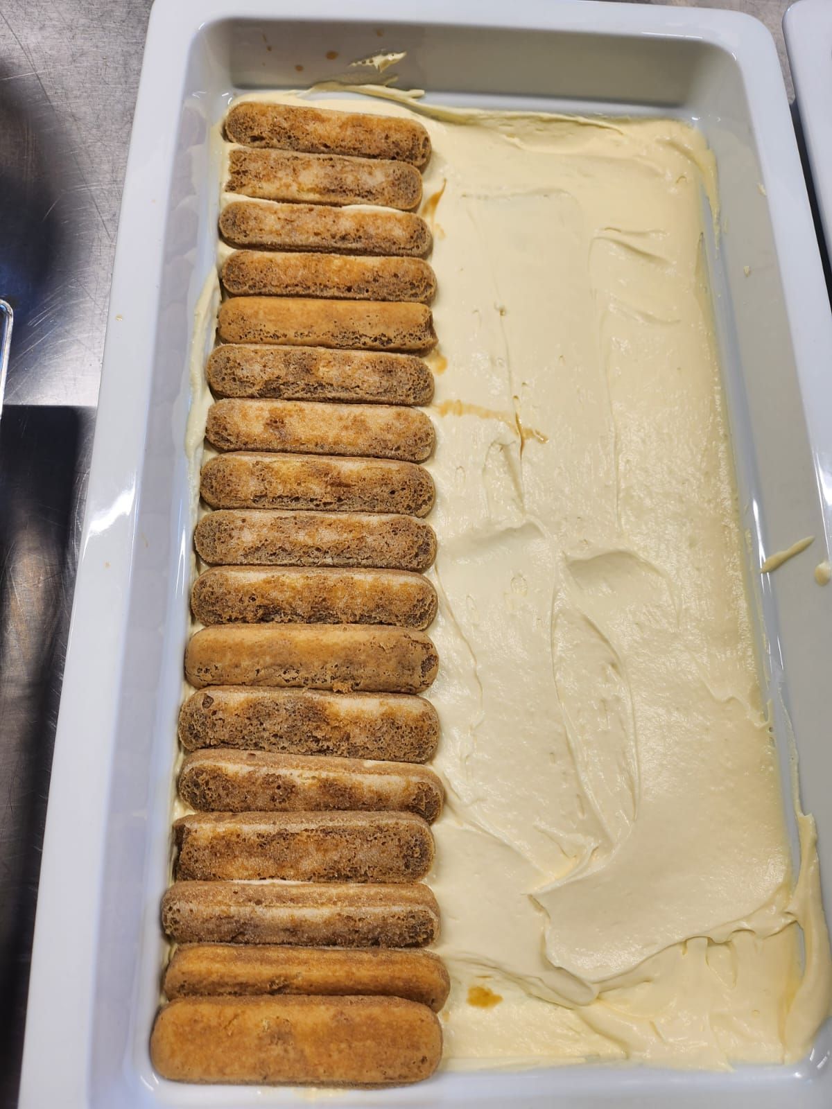 Una bandeja de tiramisú con una fila de galletas encima.
