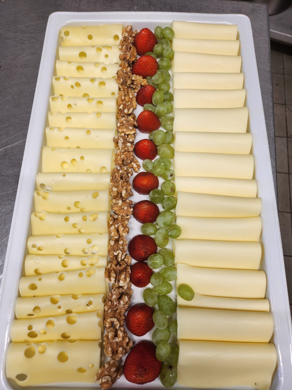 Una bandeja blanca llena de queso, fresas y uvas.