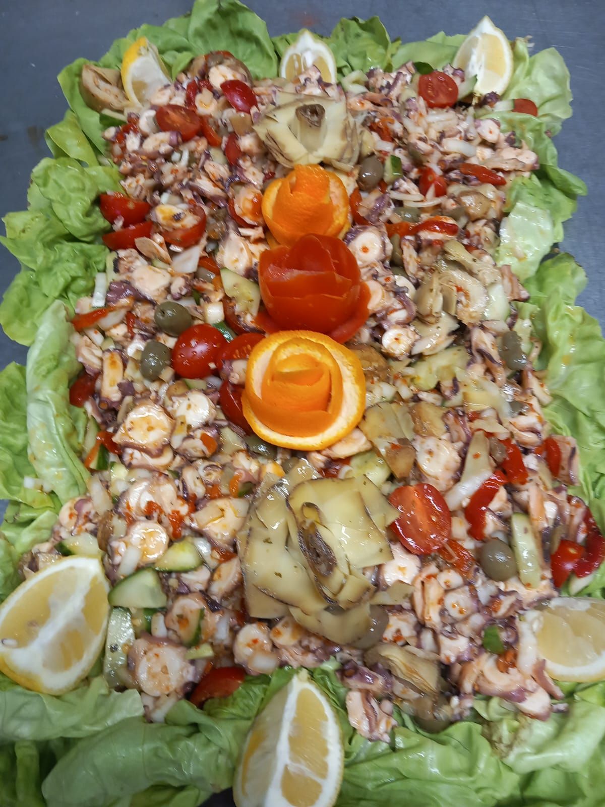 Un gran plato de comida con lechuga, tomates y limones sobre una mesa.