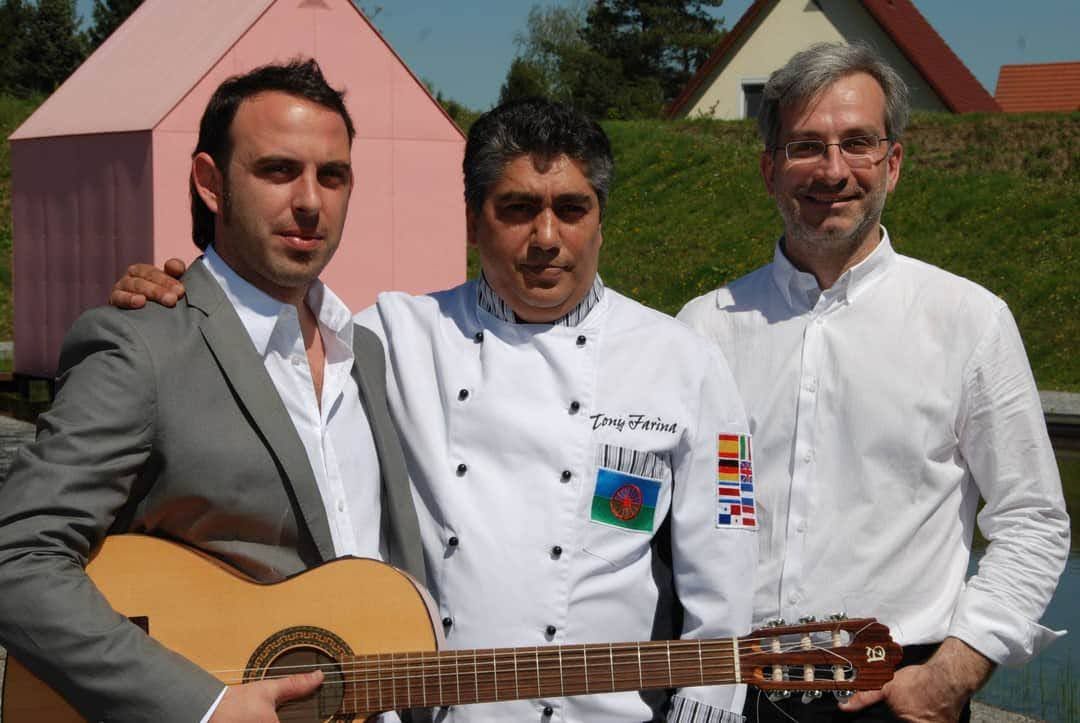 Un hombre que sostiene una guitarra posa con otros dos hombres.