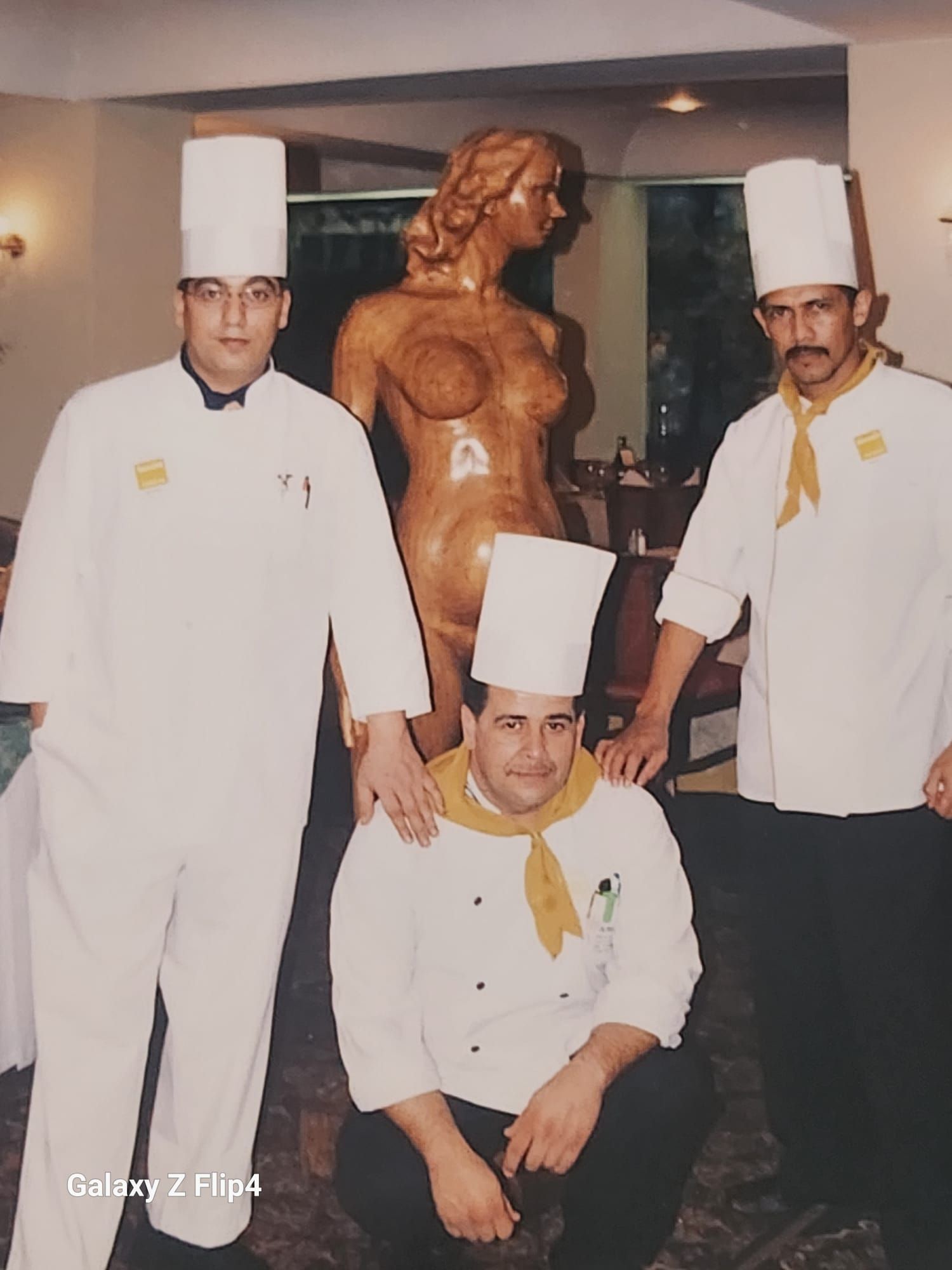 Tres chefs posan para una foto frente a una estatua