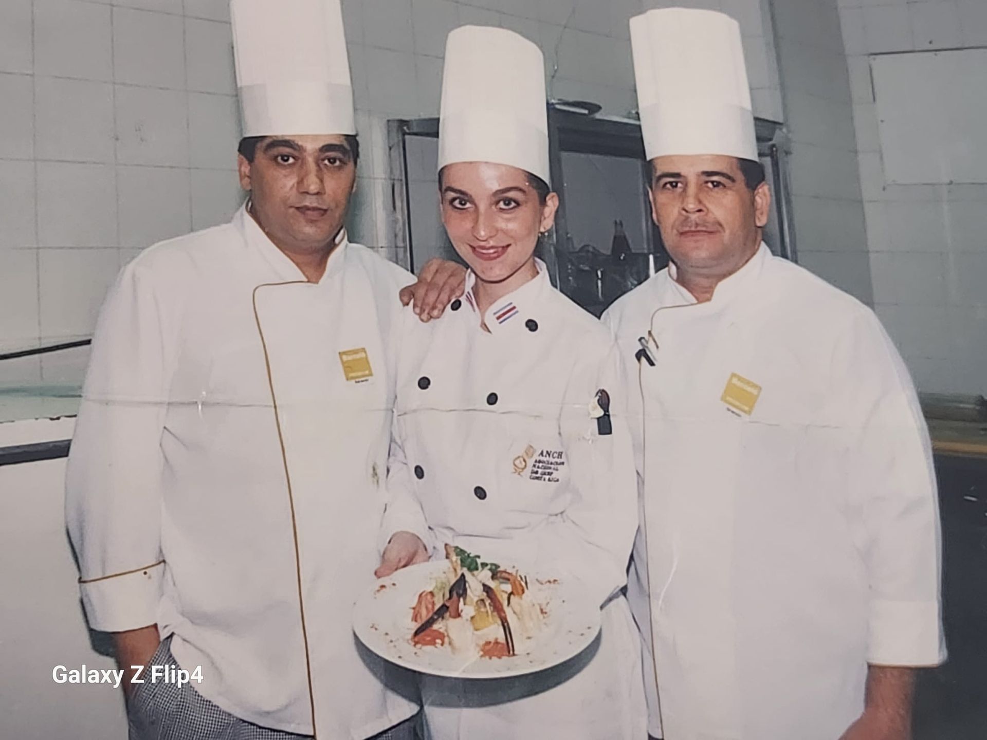 Tres chefs posan para una foto y uno de ellos sostiene un plato de comida.