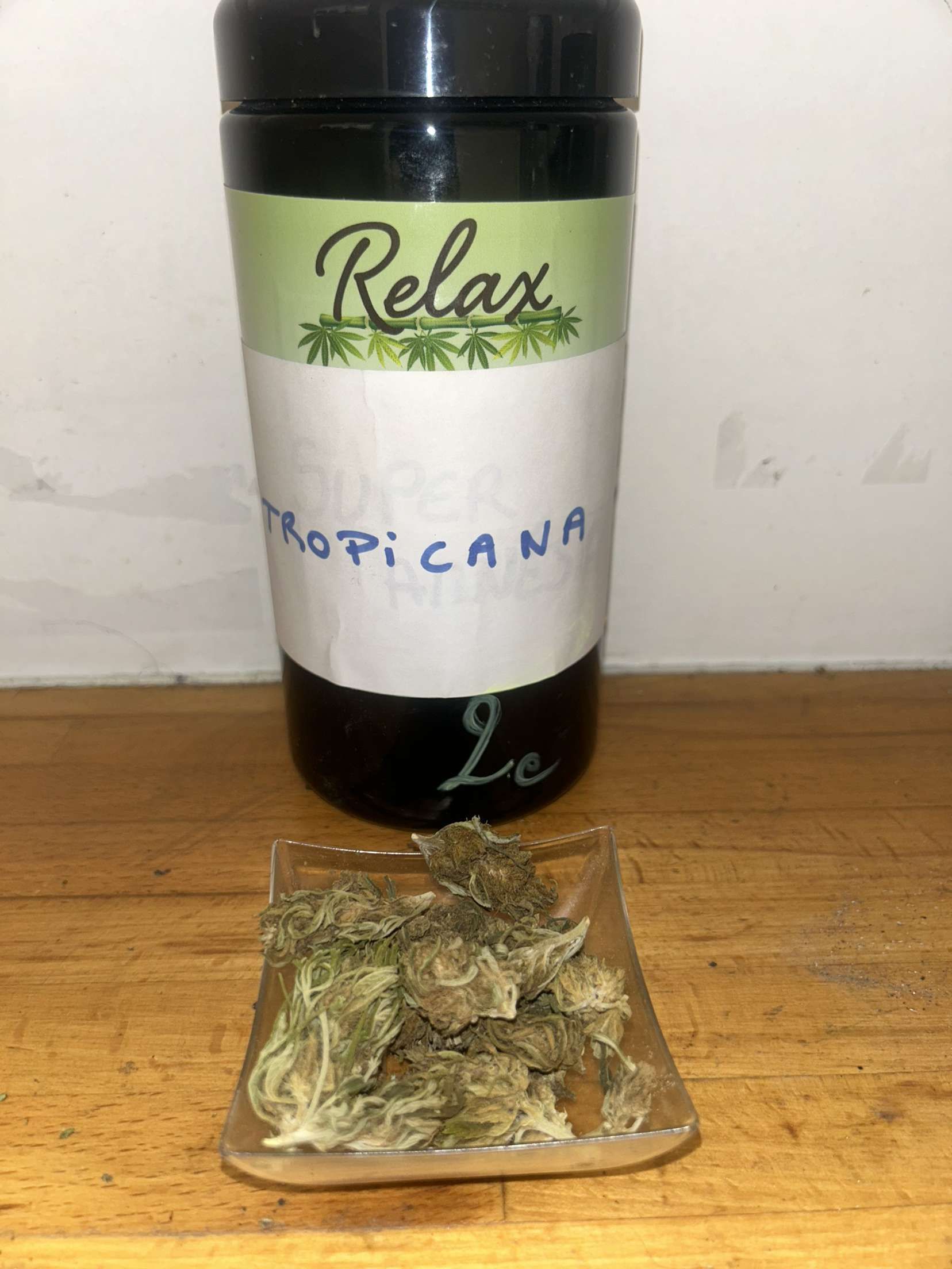 Une bouteille de Relax Tropicana est posée sur une table en bois à côté d'un petit sac d'herbe.