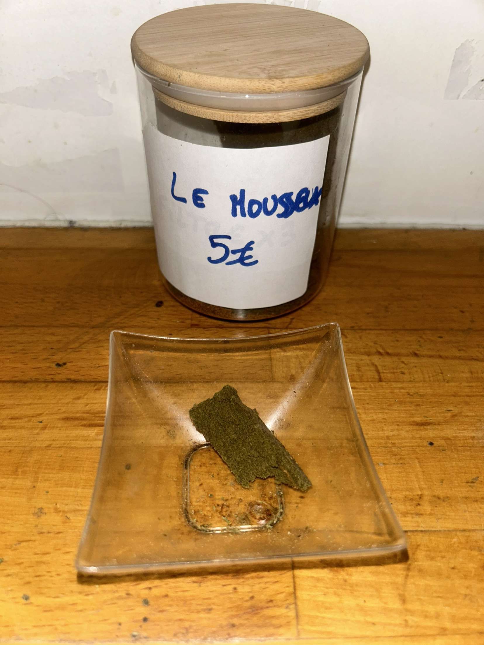 Un bocal en verre avec un couvercle en bois est posé sur une table en bois à côté d'une petite assiette carrée.