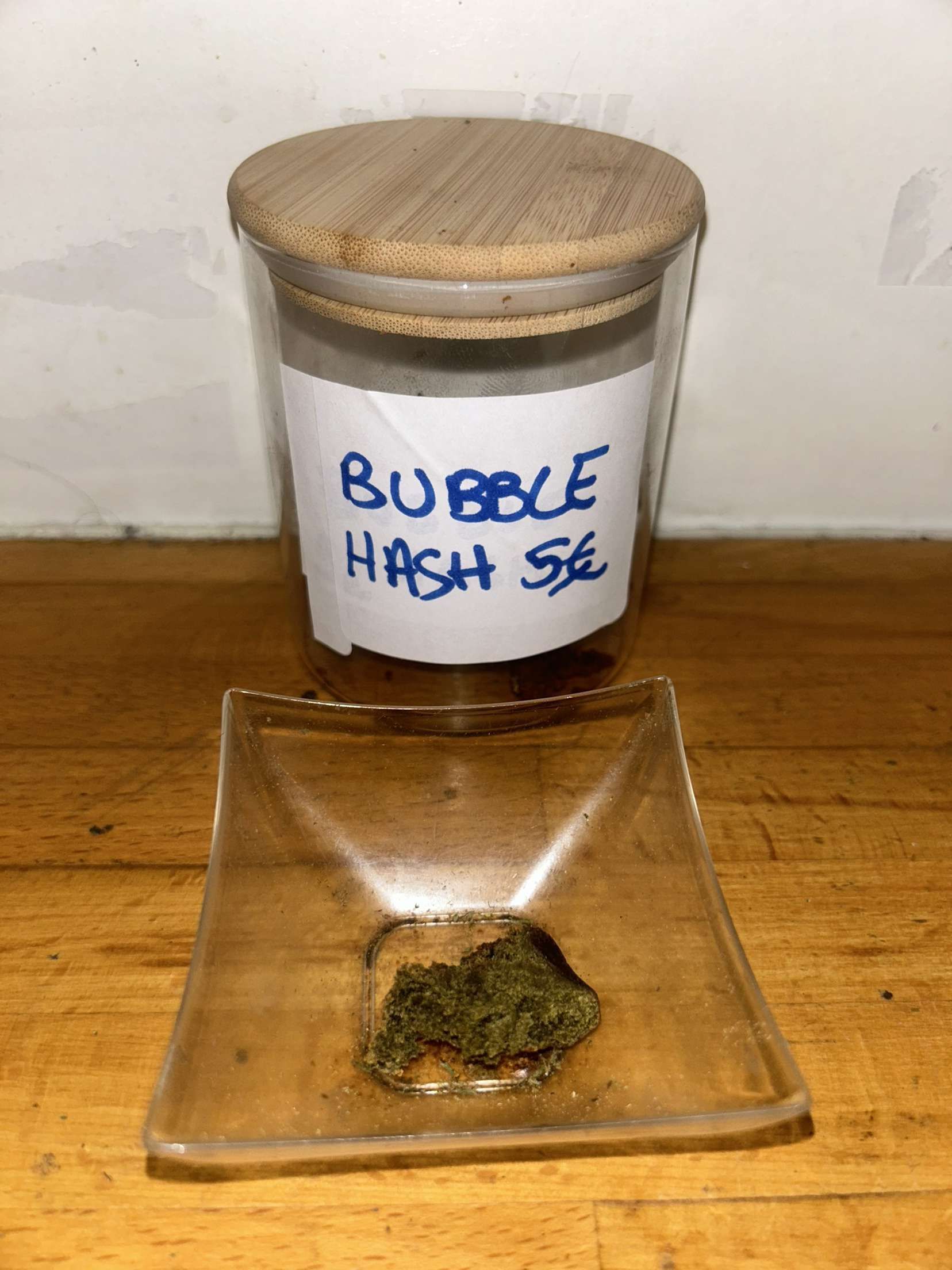 Un pot de bubble hash est posé sur une table en bois à côté d'un petit bol de bubble hash.
