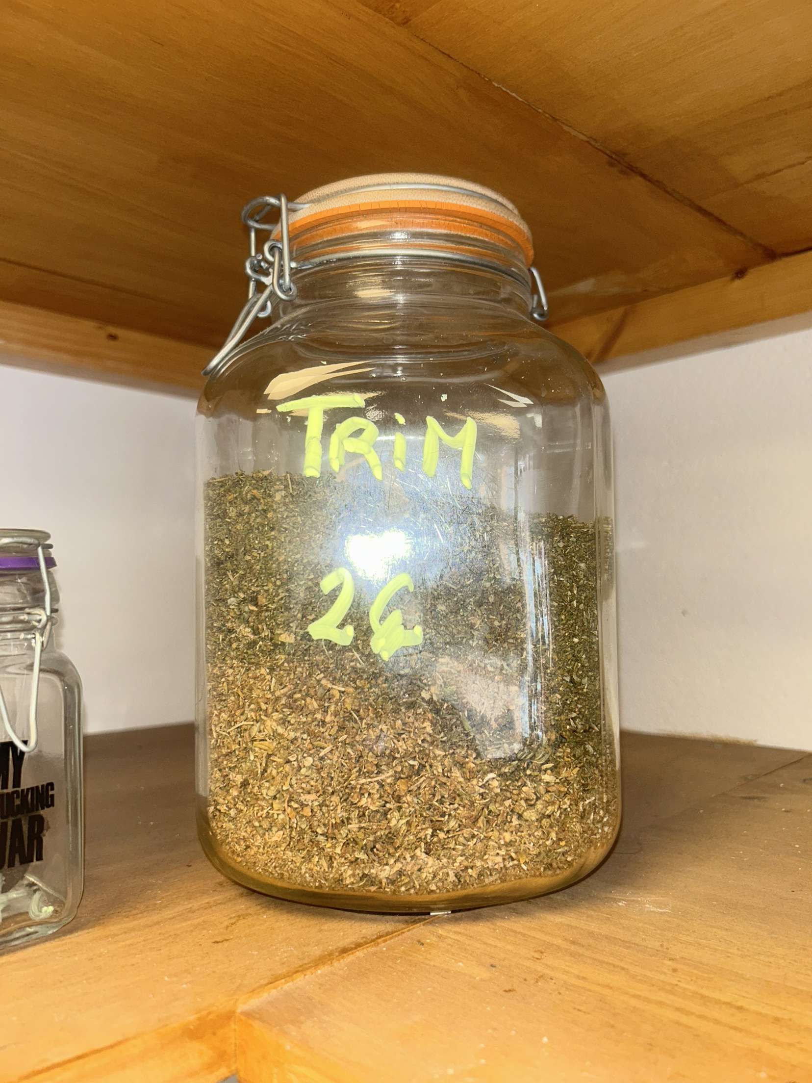 Un bocal en verre rempli d'herbes séchées est posé sur une étagère en bois.