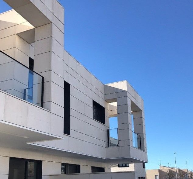 Edificio moderno, de colores claros, con diseño geométrico y balcones de cristal que se recortan contra un cielo azul.