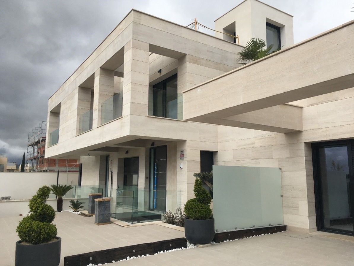 Moderna casa de piedra color beige con barandillas de cristal, grandes ventanales y jardines impecablemente cuidados.