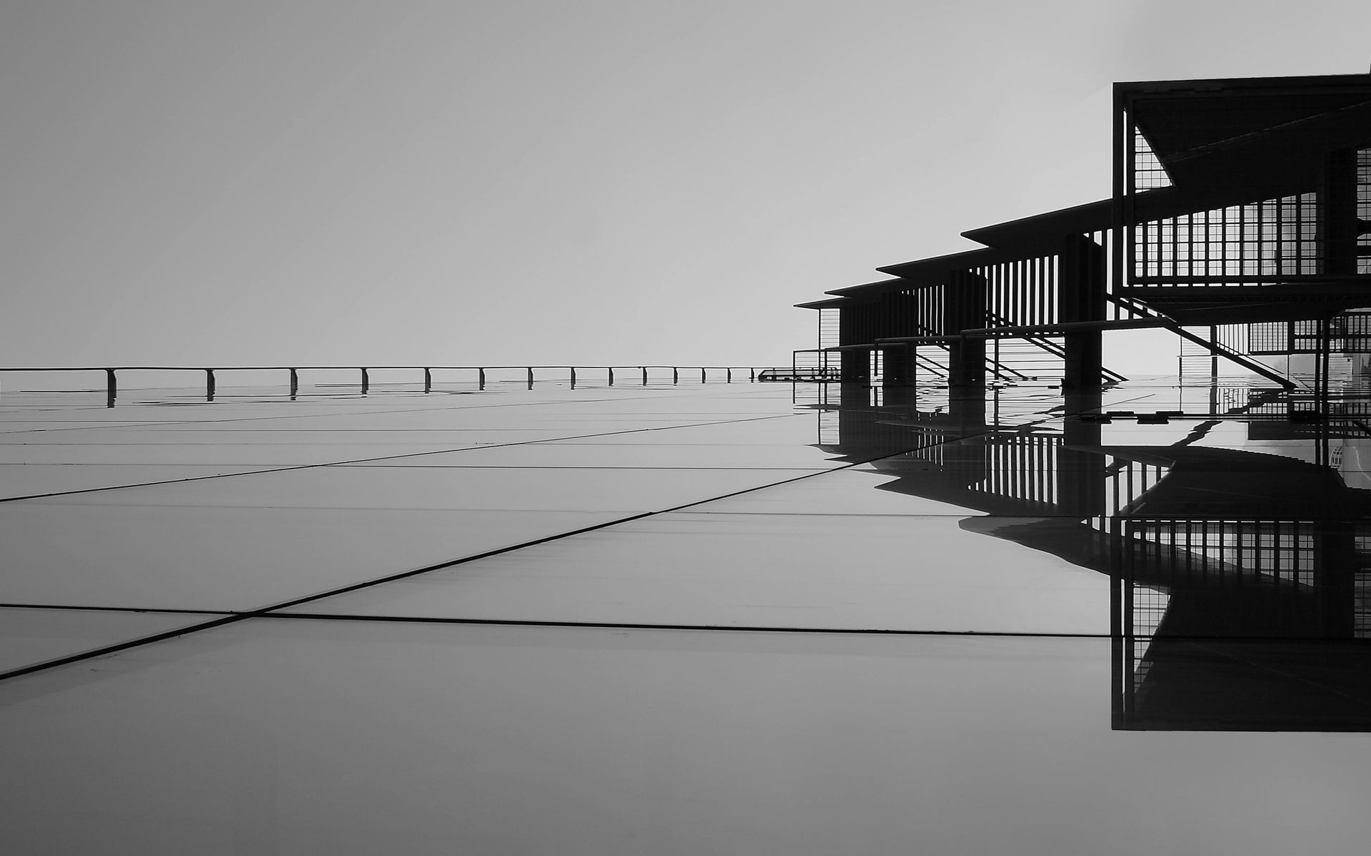 Fotografía en blanco y negro de un edificio moderno sobre el agua, reflejado en la superficie tranquila.