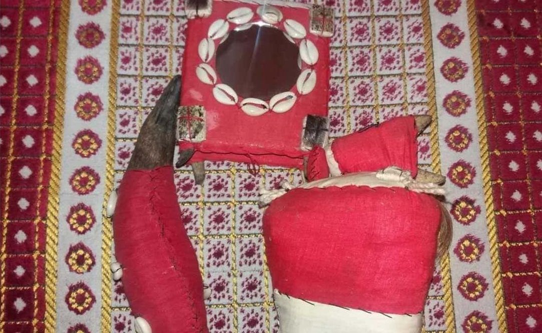 Textil ceremonial bordado en rojo y blanco, con gorro y tela a juego, sobre un fondo estampado