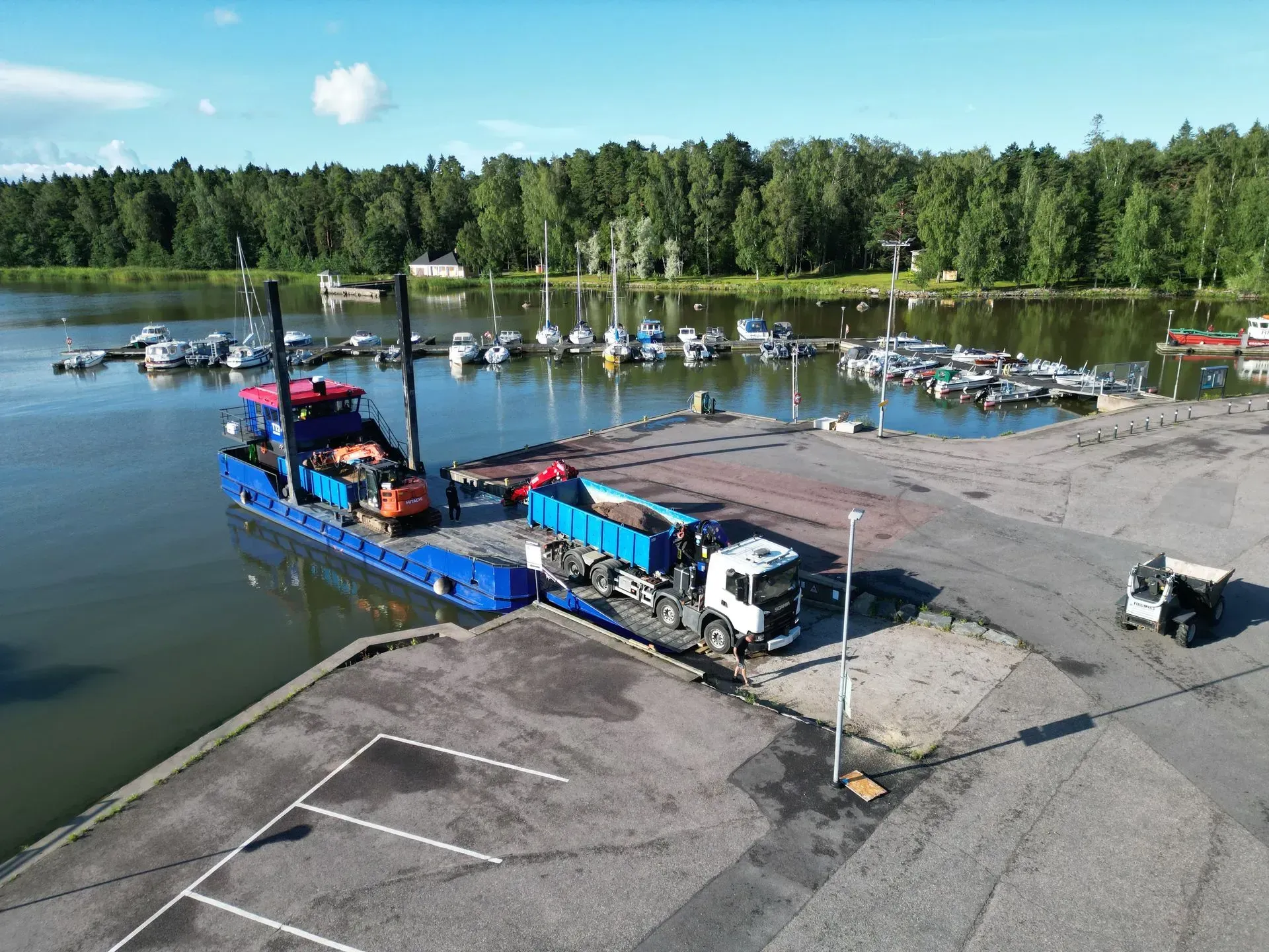 Sininen kiertoajeluvene telakoituna venesatamassa tyynen veden äärellä, taustalla monia pieniä veneitä ja puita