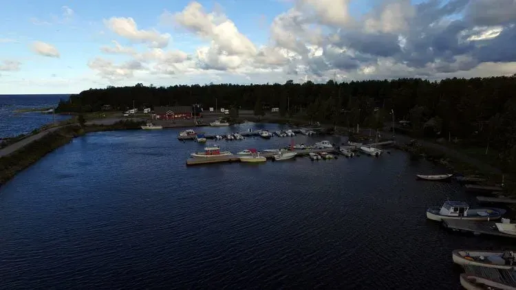 Pieni venesatama, jossa veneitä tummansinisellä vedellä pilvisen taivaan alla, puiden reunustaman rannan ympäröimänä