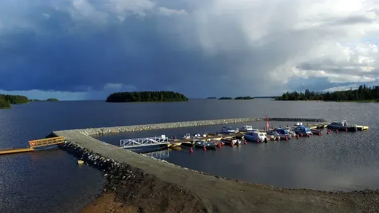 Kajakit rivissä kelluvalla laiturilla järvessä tummien ukkospilvien alla, ja kaukana siintää pieniä saaria.