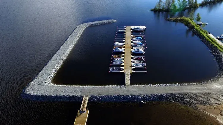 Ilmakuva pienestä venesatamasta, jossa on veneitä tummalla vedellä, jota ympäröi U-muotoinen aallonmurtaja.