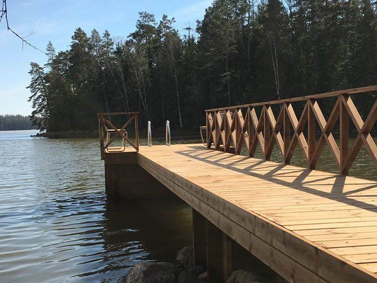 Puinen laituri, jonka ristikkäin kulkeva kaide ulottuu tyynelle järvelle metsän rannan vieressä