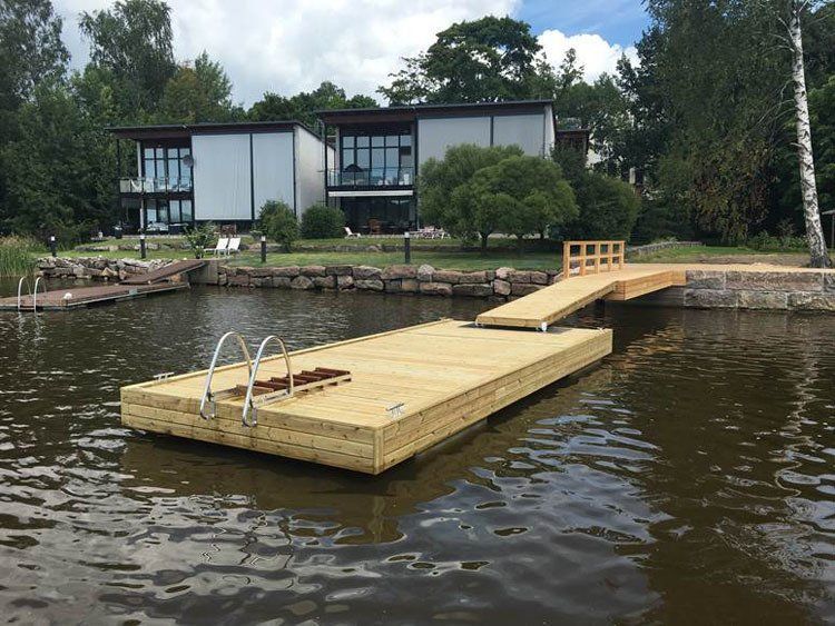 Kelluva puinen laituri järvellä modernin talon vieressä, tikkailla ja pienellä tasanteella.