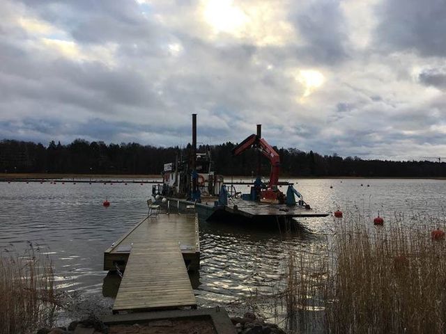 Ruoppausproomu puisen laiturin vieressä järvellä pilvisen taivaan alla