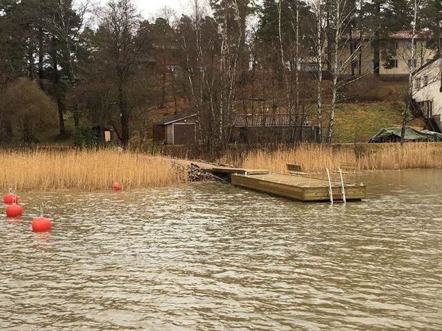 Puinen laituri aaltoilevalla järvellä, jonka rannalla on punaisia poijuja ja ruokoja