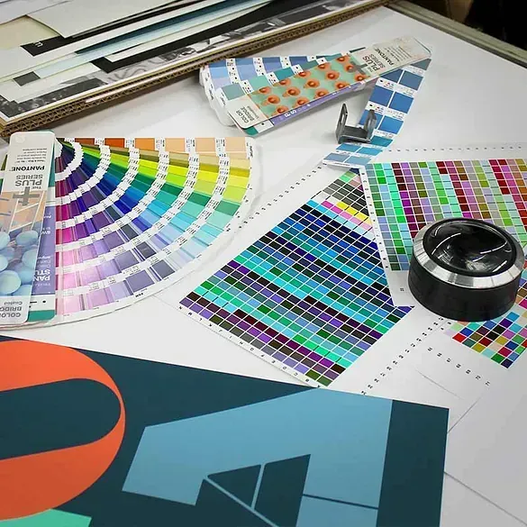 Una colección de materiales de impresión y diseño con muestras de color, muestras y una lupa sobre una superficie blanca.