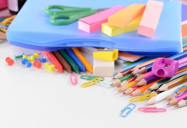 Un estuche azul lleno de útiles escolares, incluidos lápices, borradores, tijeras y clips para carpetas.
