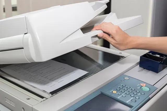 Una persona está usando una fotocopiadora para escanear una hoja de papel.