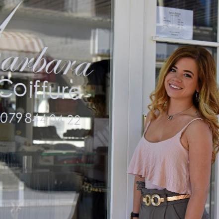 une femme blonde au cheveu long se tient devant un salon de coiffure