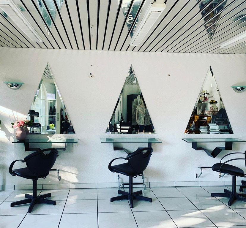 vue intérieure d'un salon de coiffure avec trois fauteuils devant des miroirs triangulaires