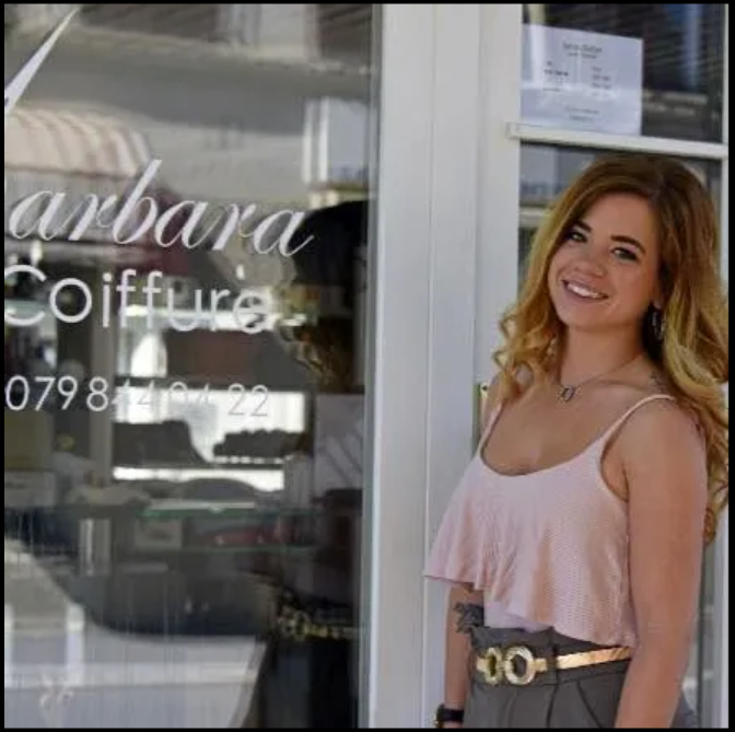 Une femme au cheveux long et blond pose devant un salon de coiffure