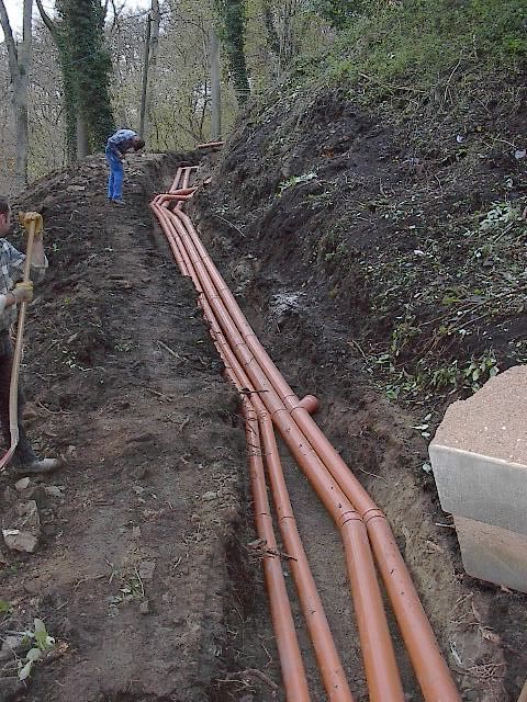 Arbeiter verlegen braune Rohre in einem Graben an einem Hang.