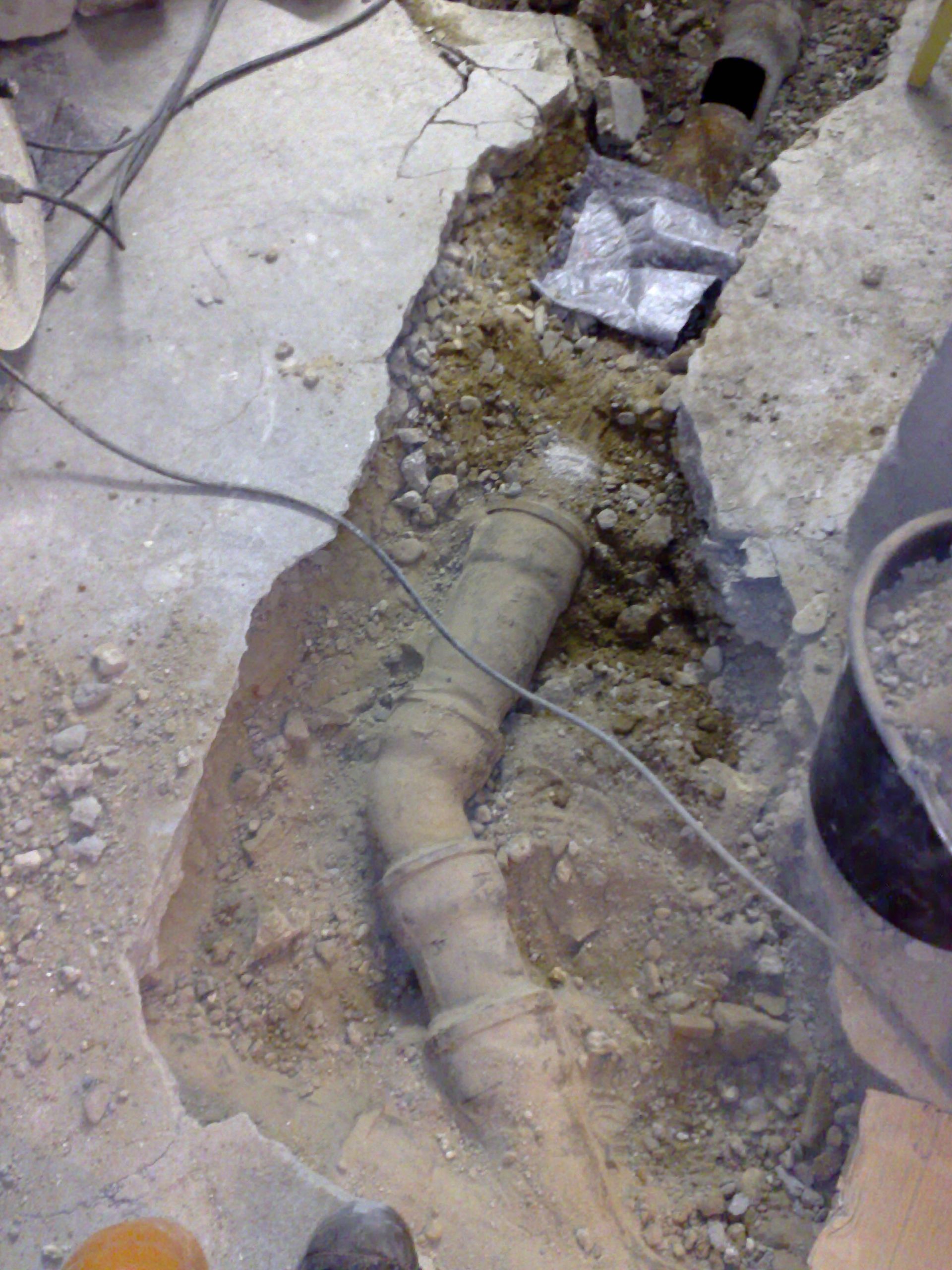 In einem aus Beton gegrabenen Graben liegen freiliegende Wasserleitungen. Umgeben von schmutzigem, braunem Boden.