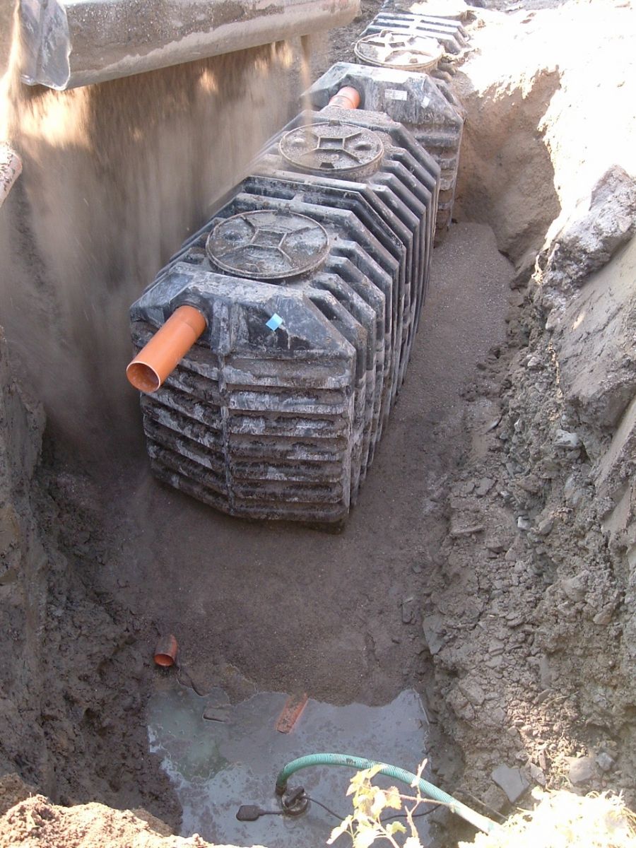 Eine rechteckige schwarze Klärgrube in einem ausgehobenen Graben, verbunden mit einem orangefarbenen Rohr.