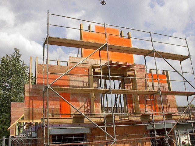 Außenansicht des Gebäudes im Bau mit Gerüst und orangefarbenen Ziegeln.