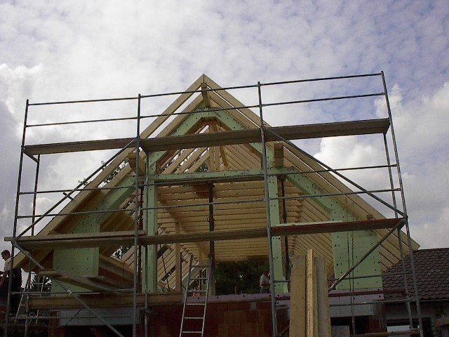 Baustelle: Holzdachstuhl mit Gerüst, vor bewölktem Himmel.
