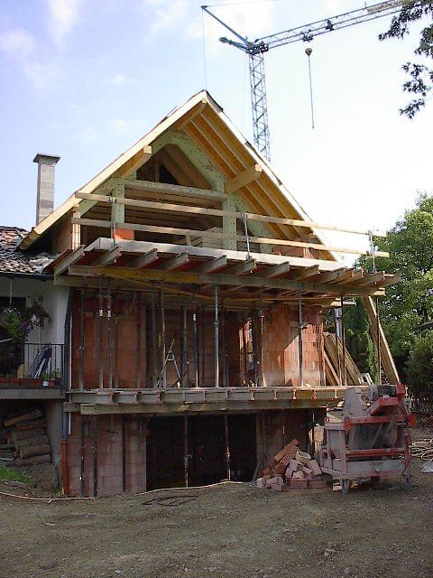 Haus im Bau, mit Holzrahmen, Gerüst und einem Kran darüber.