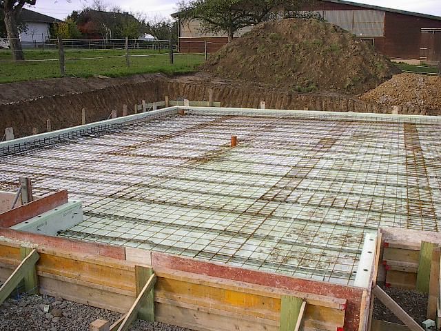 Baustelle mit Holzschalung, Bewehrung und Isolierung, vorbereitet für das Betonieren des Fundaments.