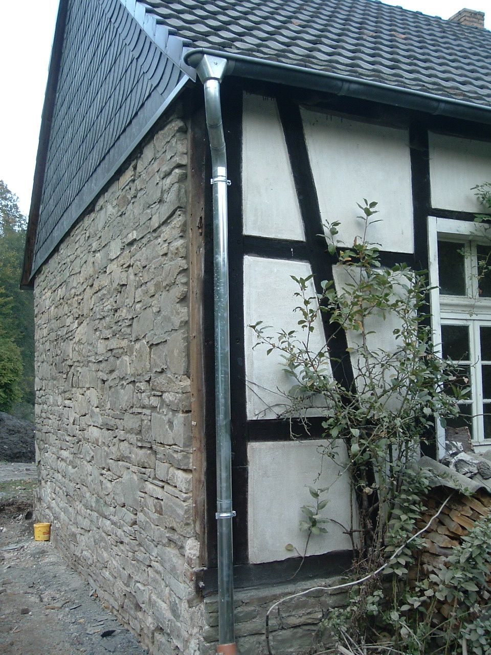 Stein- und Fachwerkhaus mit einem Metallfallrohr an der Ecke. Schieferdach und Kletterpflanze.