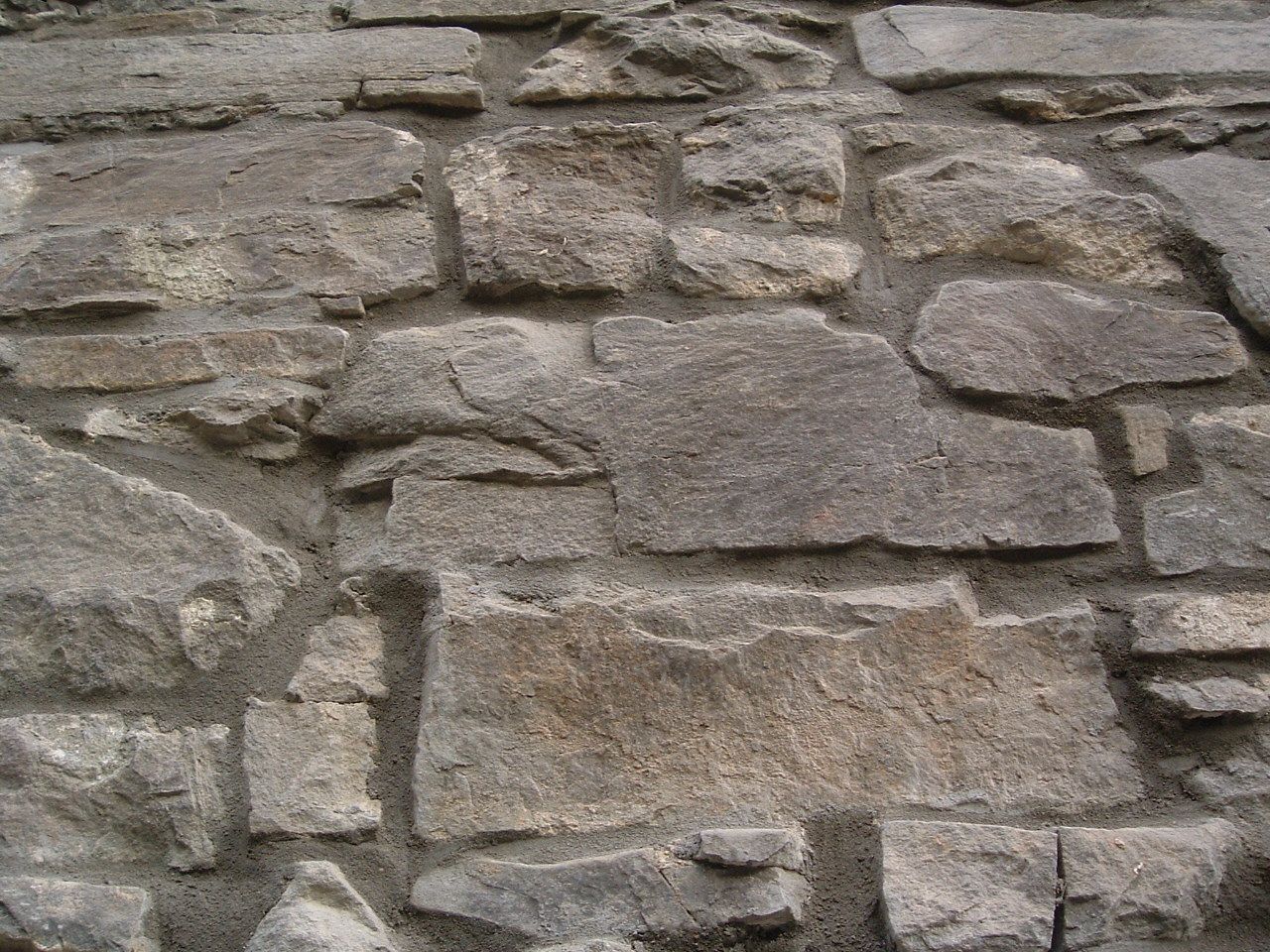 Steinmauer mit unterschiedlichen Größen und Grautönen, strukturierte Oberfläche.