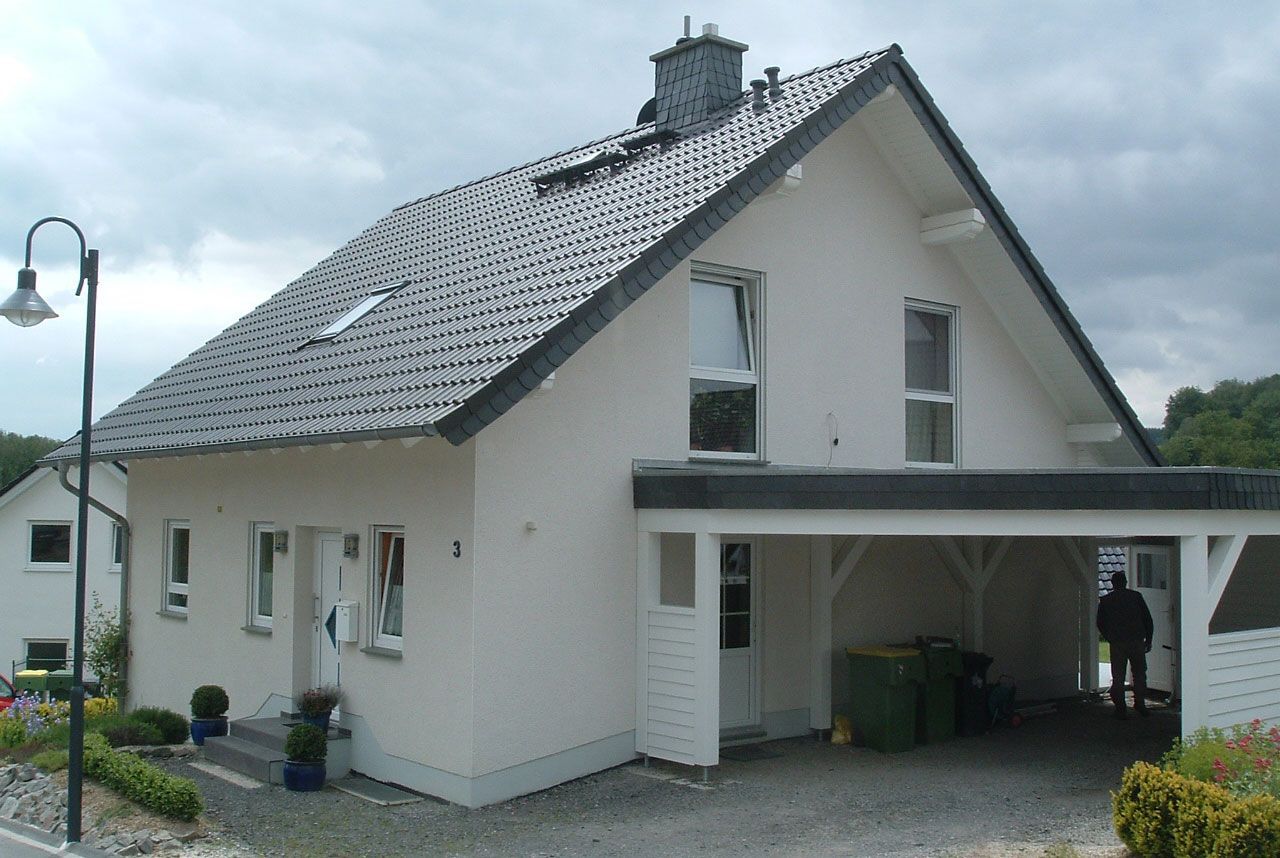 Weißes Haus mit dunklem Dach, Carport und Straßenlaterne an einem bewölkten Tag.