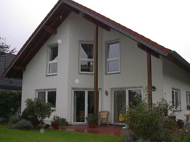 Zweistöckiges Stuckhaus mit braunen Verzierungen, großen Fenstern und einem roten Ziegeldach, umgeben von einem grünen Rasen.