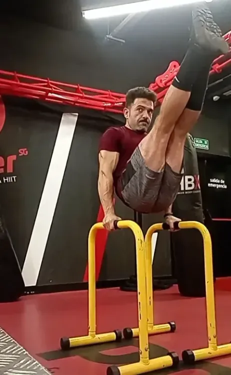 Un hombre está haciendo una parada de manos en barras paralelas en un gimnasio.