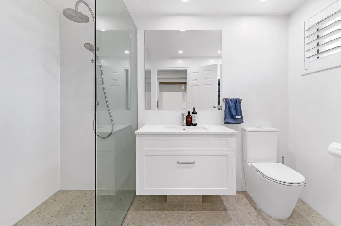 A bathroom with a toilet , sink , mirror and walk in shower.