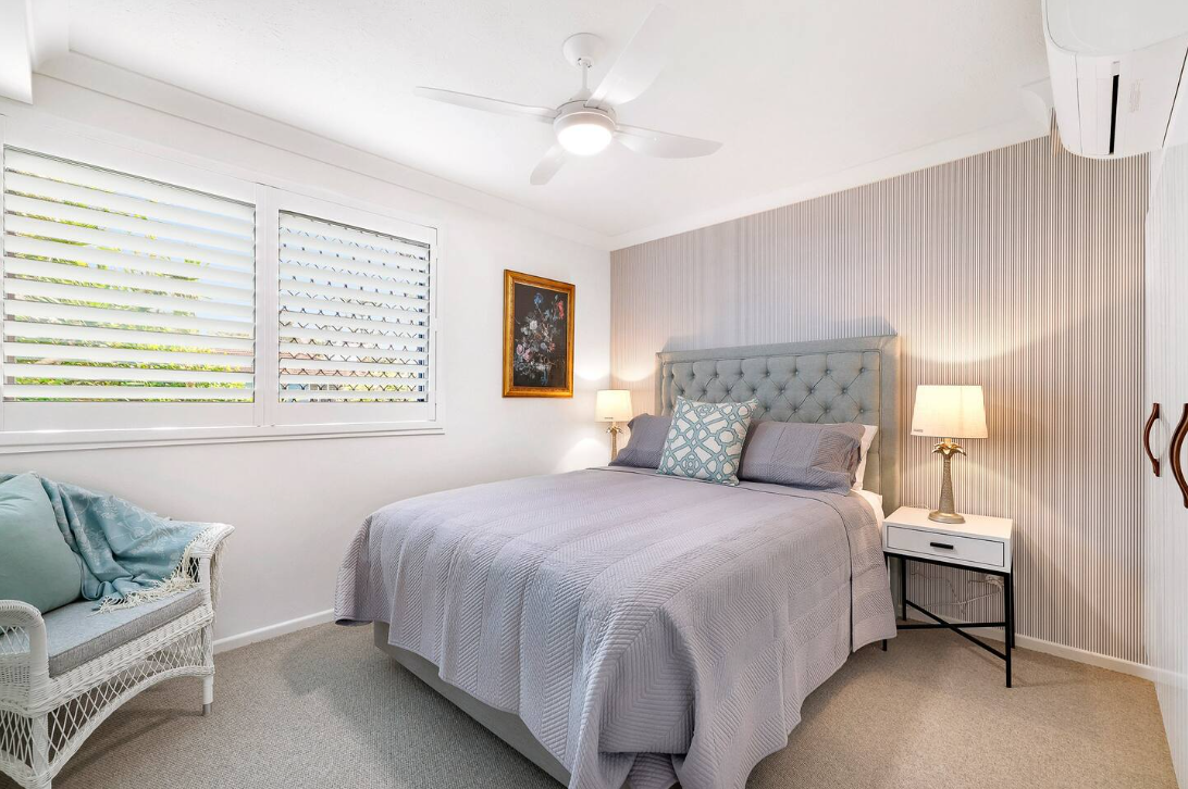 A bedroom with a bed , nightstand , chair and ceiling fan.