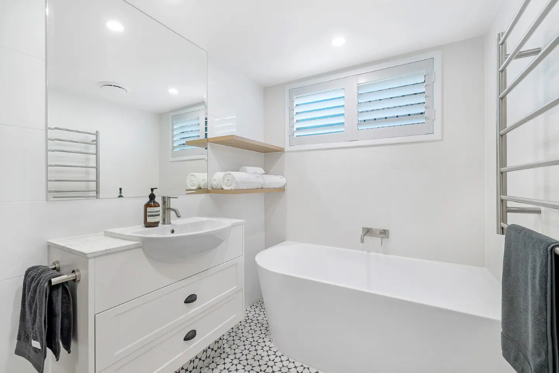 A bathroom with a tub , sink , mirror and window.