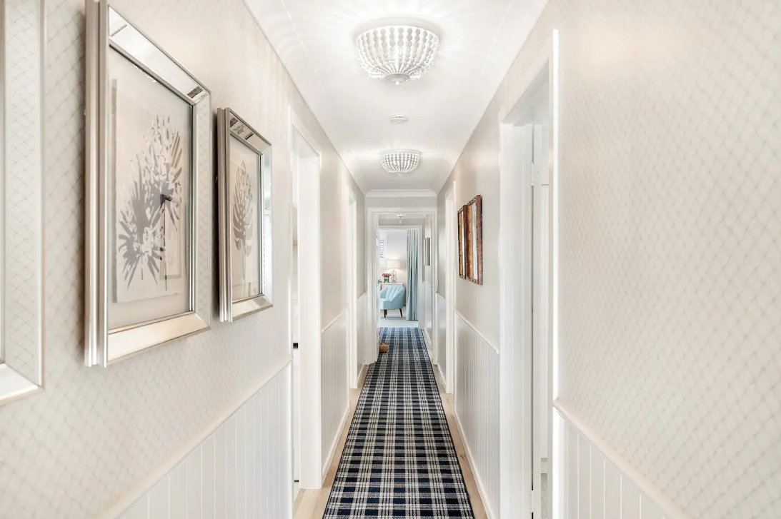 A long hallway with a blue and white checkered rug and paintings on the wall.
