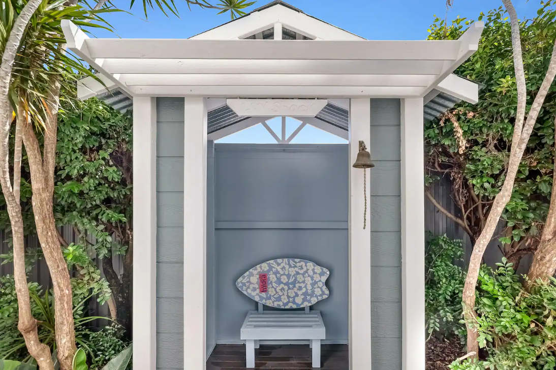 A white pergola with a bench and a surfboard on the wall.