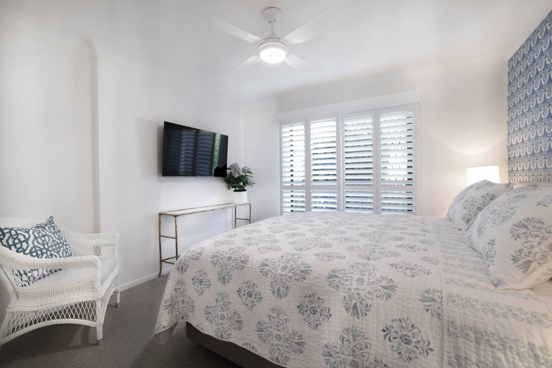 A bedroom with a king size bed , chair , television and ceiling fan.