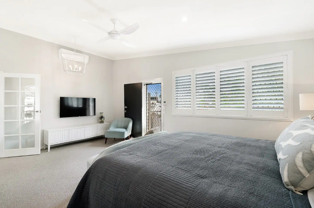 A bedroom with a bed , chair , television and shutters.