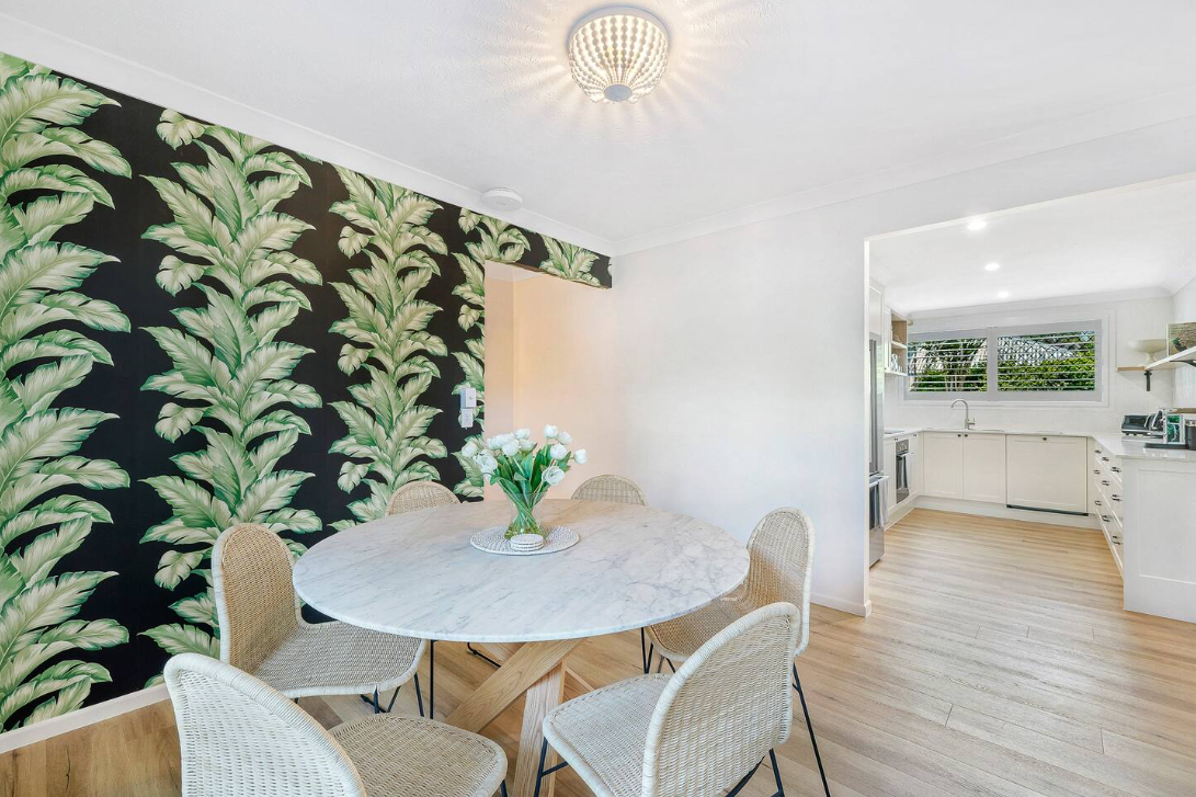 A dining room with a table and chairs and a vase of flowers.