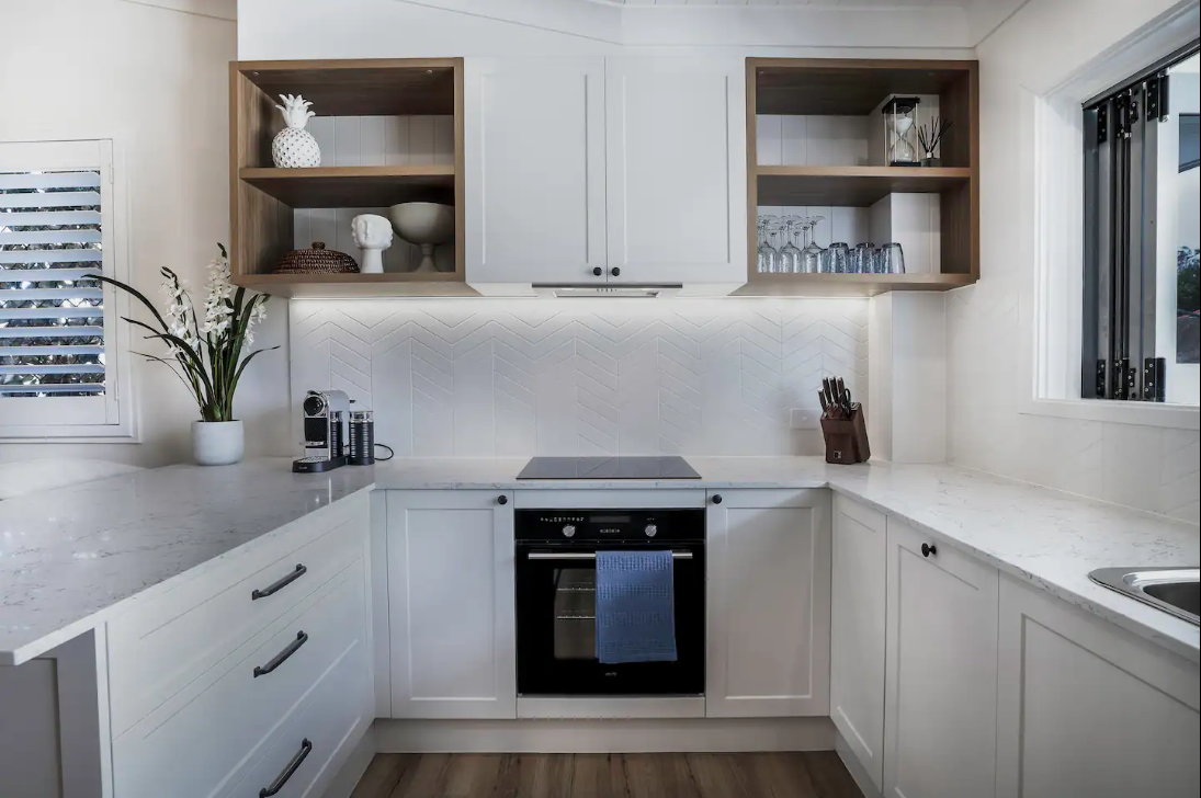 A kitchen with white cabinets , a stove , a sink , and a window.